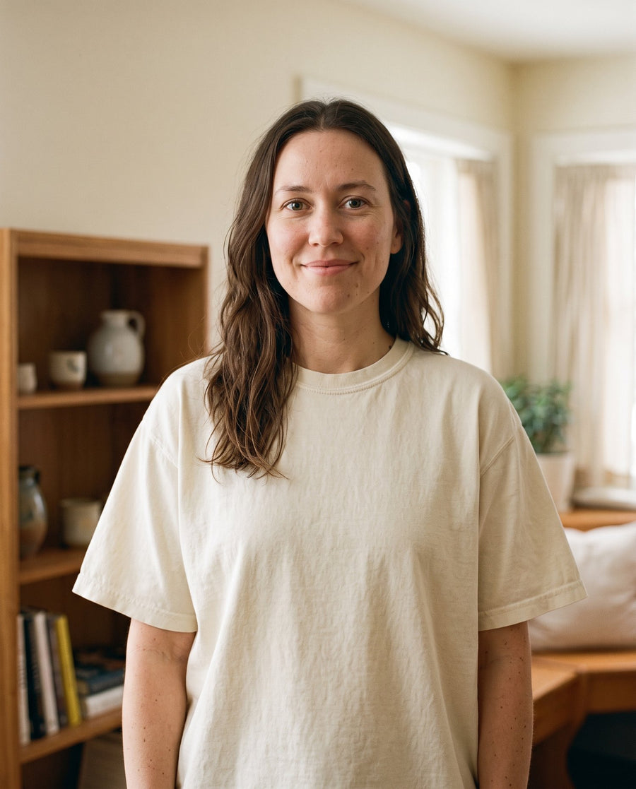 A woman smiling warmly at the camera in a cream Prayer Moms garment-dyed cotton tee in her sunlit home