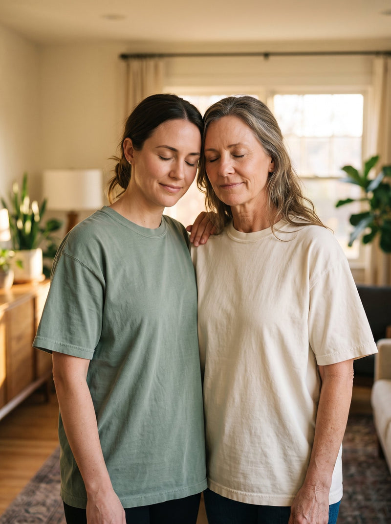 Two women praying together, one hand resting on the other's shoulder, in sage and cream Prayer Moms tees